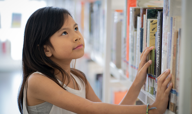 Young girl looking at books on a bookshelf