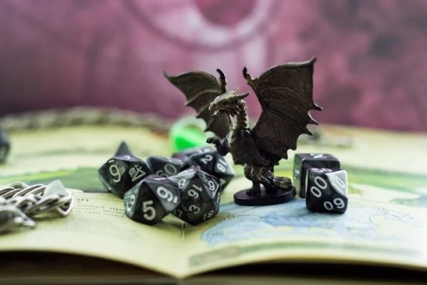 A dragon figurine perched atop a book, surrounded by a set of dice.