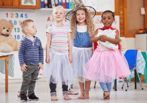 Four children standing in a classroom, each child wearing a costume, they are smiling and laughing. 